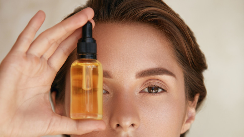 woman holding a bottle of facial oil to one eye