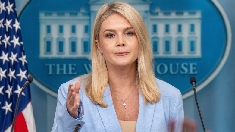 Karoline Leavitt in press room with White House logo behind her, gesturing with one hand and pursed lips