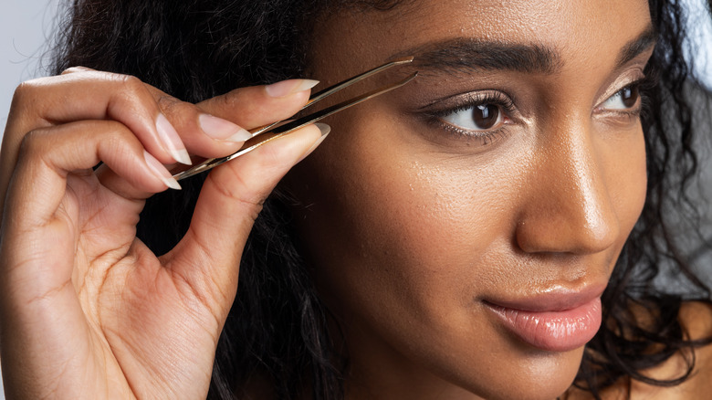 Black woman using tweezers on the end of her brows