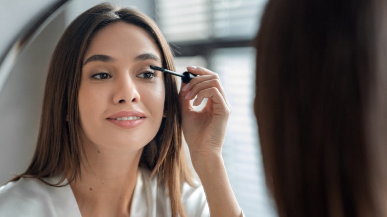 woman using mascara in mirror