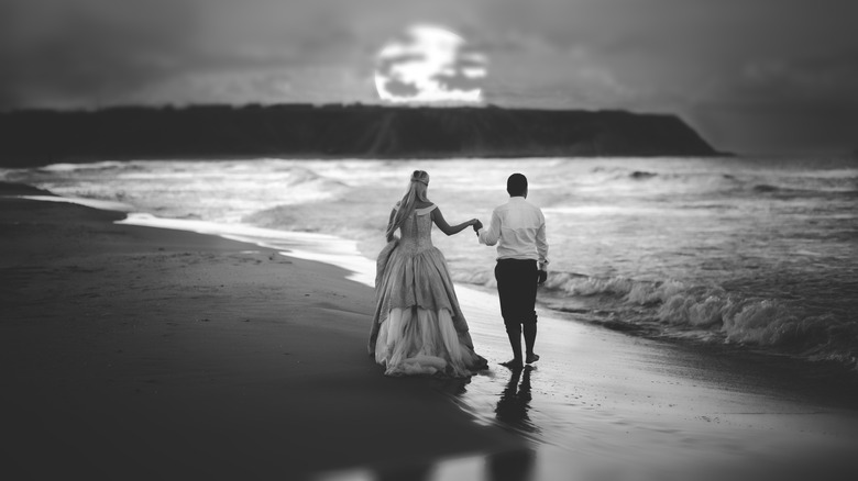 Black and white photo of bride and groom walking on the beach