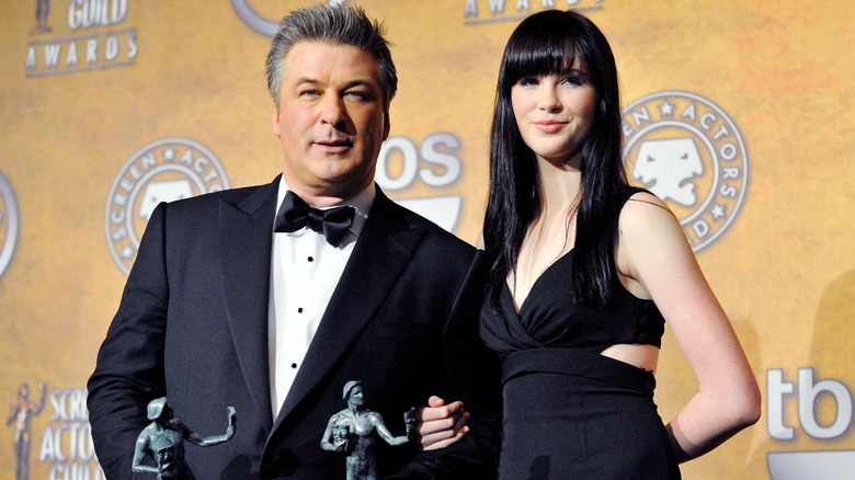 Alec Baldwin holding two SAG Awards statuettes and and linking arms with Ireland Baldwin.