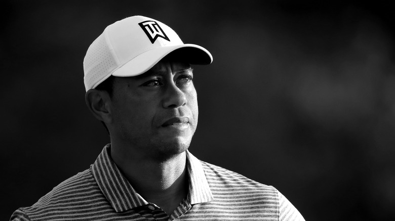 Black and white photo of Tiger Woods wearing a white cap and striped polo shirt
