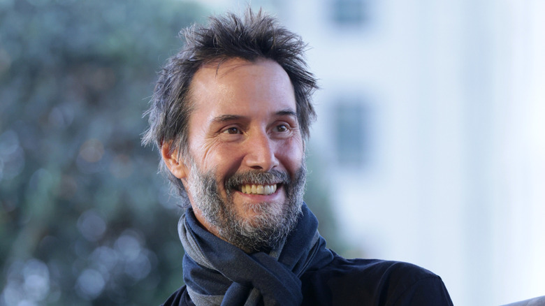 Keanu Reeves with a salt-and-pepper beard wearing a blue muffler