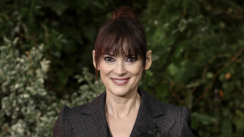 Winona Ryder in a checked blazer against leafy background