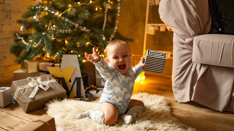 Baby smiling and holding present in front of Christmas tree