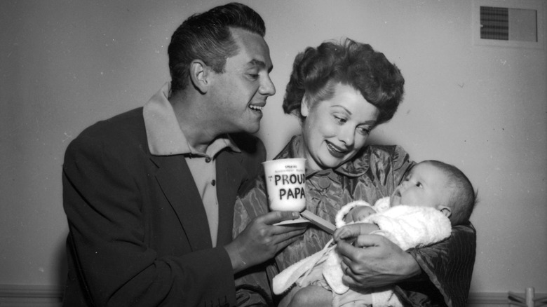 Lucille Ball at home with her husband Desi Arnaz and their son Desi Jr., 1953. Desi Sr. is holding a mug with the caption 'Proud Papa' on it.