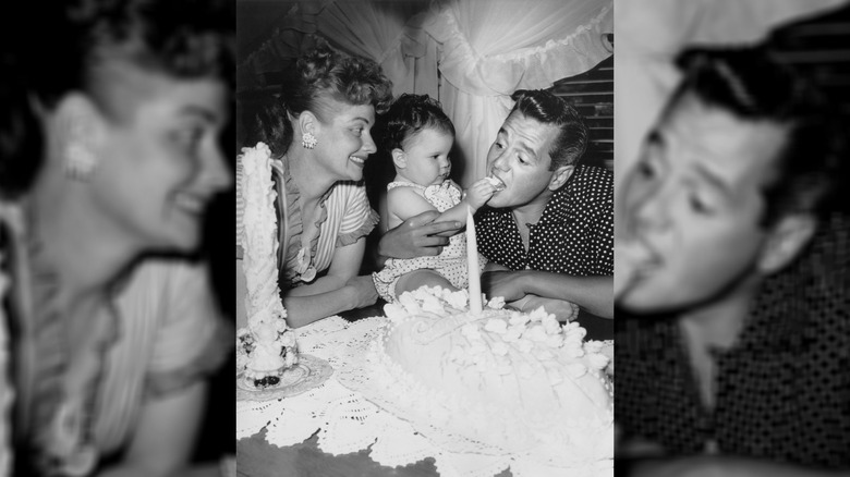 A year old Lucie Arnaz feeds her father, Desi Arnaz, some cake on her birthday. Lucille Ball watches on, smiling.