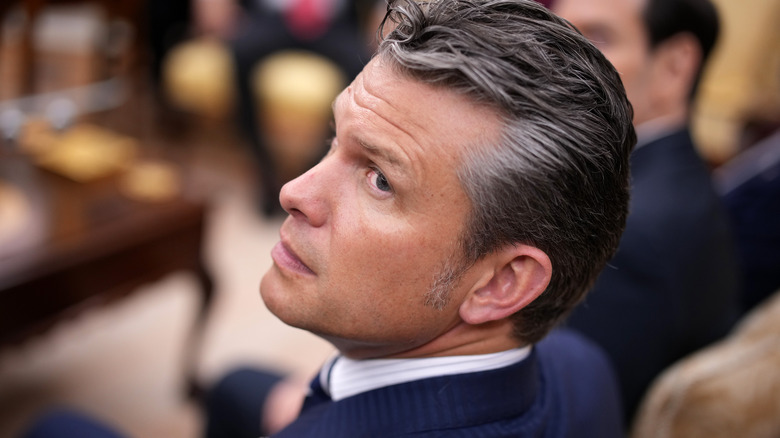 Pete Hegseth looking over his shoulder in a navy suit