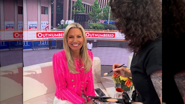 Ainsley Earhardt in a pink blazer, getting her makeup done.
