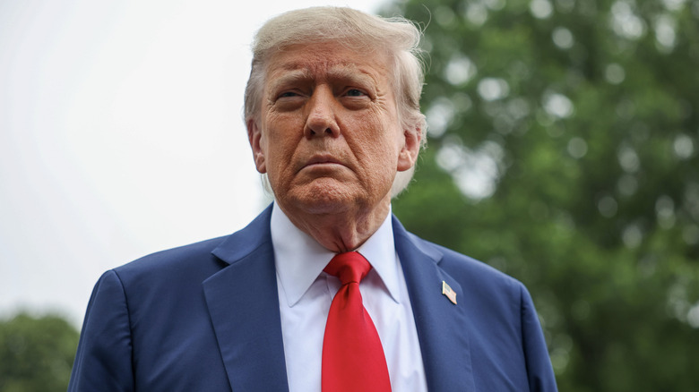 Donald Trump stands outdoors, looking up and frowning