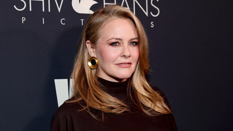 Alicia Silverstone poses on the red carpet for the Women in Film Oscar Nominees Celebration in March 2026 wearing gold earrings with a large, black stone in the center