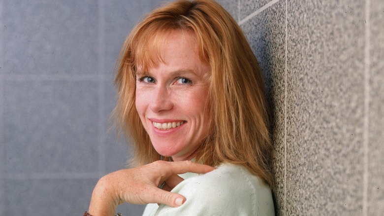 Amy Madigan with her hand on her shoulder in front of a tile wall