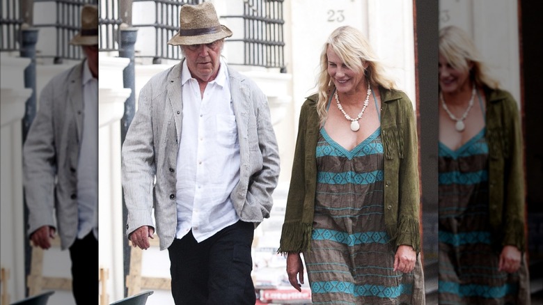 Daryl Hannah in striped deress and olive jacket walking with Neil Young in a hat and white shirt