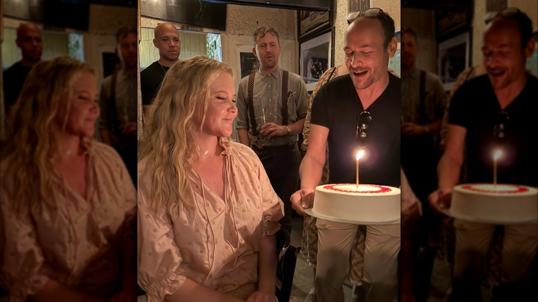 Amy Schumer in a restaurant wearing a peasant blouse while a man carries a cake with a lit candle