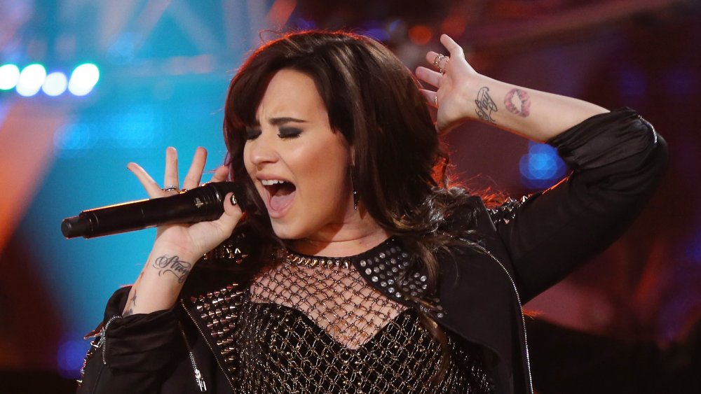 Demi Lovato performing in 2012 with her "stay strong" tattoos visible