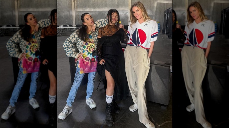 Janel Parrish wearing a tie-shirt and sweater while posing with her "Stockholm Squad" costars.