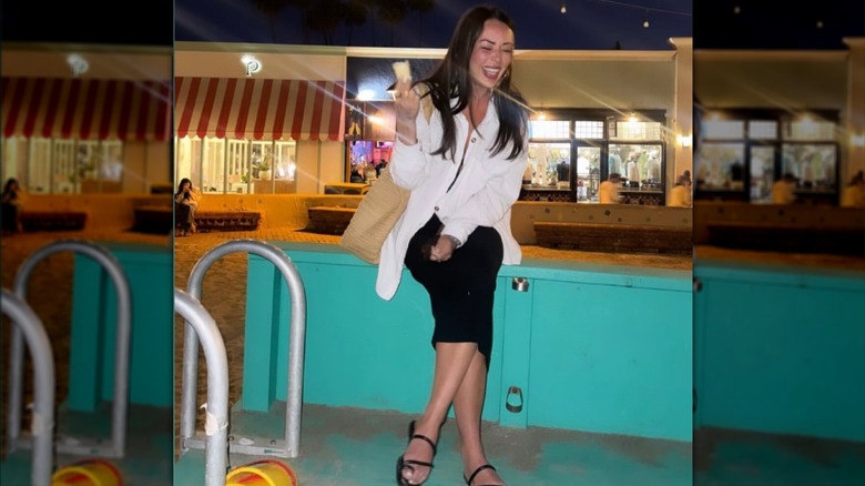 Janel Parrish sitting on a railing and laughing.