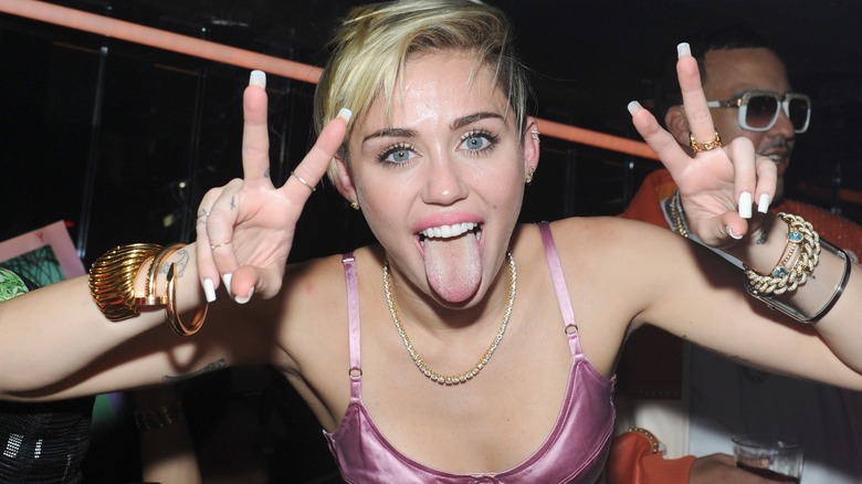 A blonde Miley Cyrus flashing peace signs and sticking out her tongue