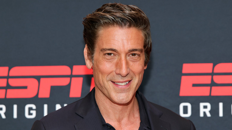 David Muir, dressed in black, in front of the ESPN logo