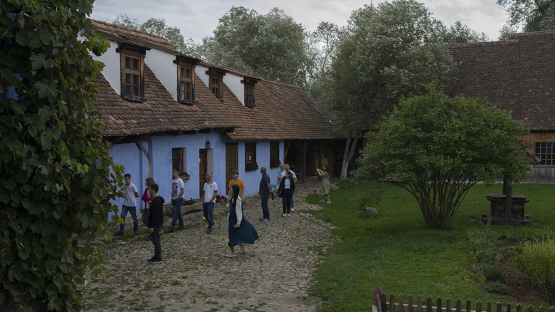 King Charles' traditional Saxon farmhouse in Transylvania, Romania. A white cottage with a slate roof sat in a garden with trees to the right and a steep hill to the left