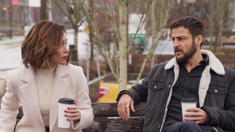 Autumn Reeser and Tyler Hynes sitting on a bench holding coffee cups