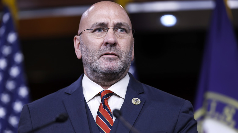 Clay Higgins addressing a crowd in a navy suit and glasses