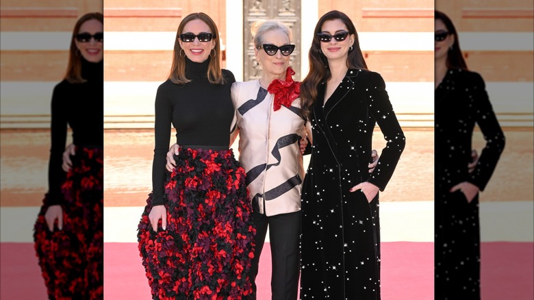 Emily Blunt, Meryl Streep, and Anne Hathaway wearing sunglasses and smiling together.