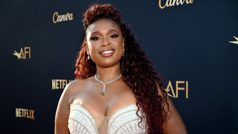 Jennifer Hudson smiling on the red carpet at an event in front of a dark background