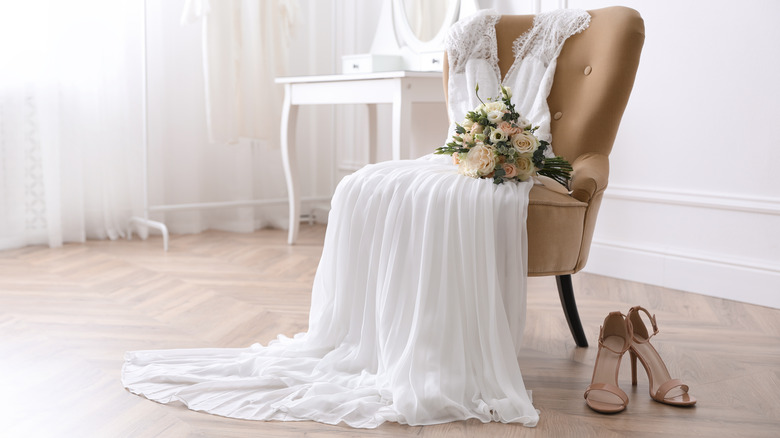 bridal bouquet on top of a wedding dress draped over a chair