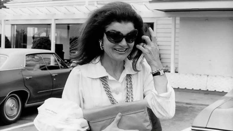 Jackie Kennedy Onassis smiling and tucking hair out of her face in 1975