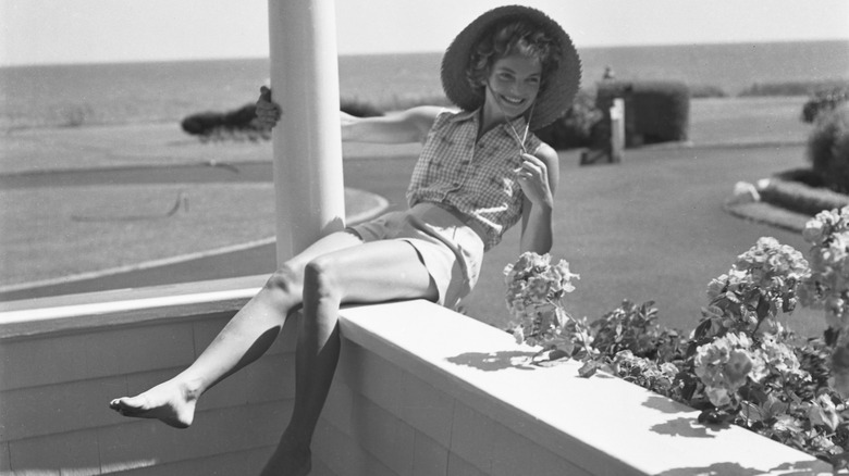 Jackie Kennedy leaning back over a porch and holding onto a pillar