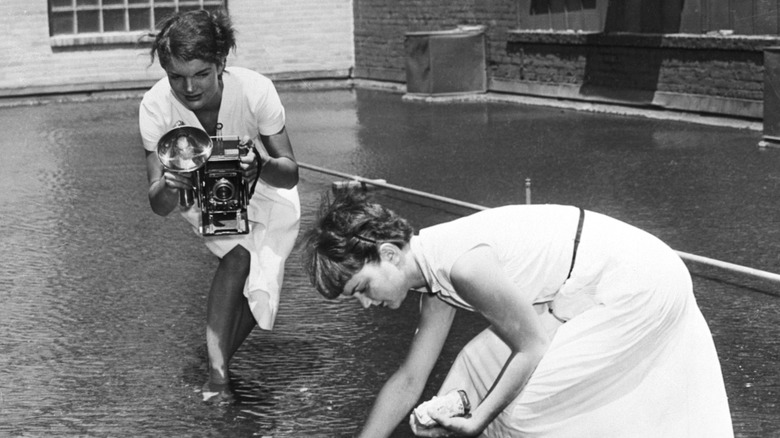Jackie Kennedy with her feet submerged in water and photographing a woman
