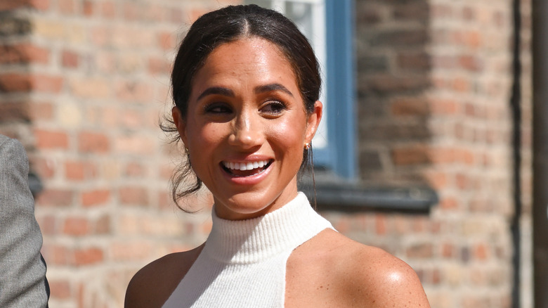 Smiling Meghan Markle wearing white halterneck seater
