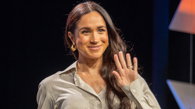Smiling Meghan Markle waving and wearing a striped taupe shirt