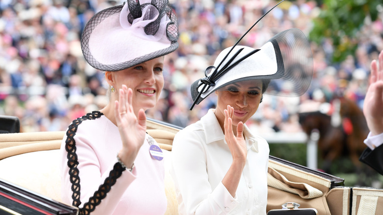 Meghan Markle and Duchess Sophie waving at a crowd during a carriage ride