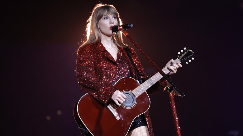 Taylor Swift in a red blazer with a red guitar on stage
