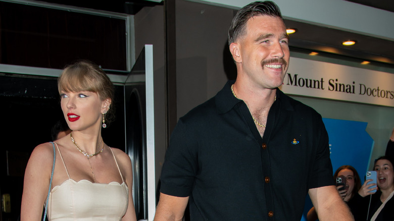 Taylor Swift and Travis Kelce walking out of a building in New York with Taylor in a cream sleeveless dress
