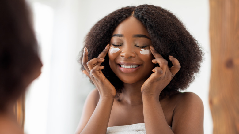 woman in towel applying eye cream 