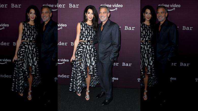 Amal Clooney in a polka dotted dress with George Clooney on a carpet.