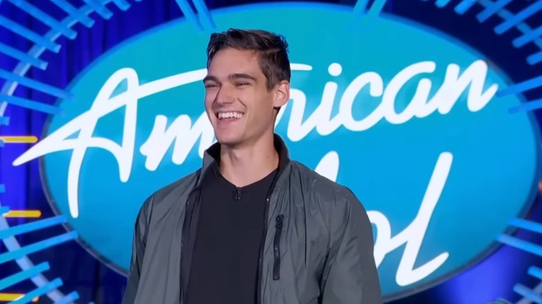 Nick Merico smiling in front of the American Idol logo