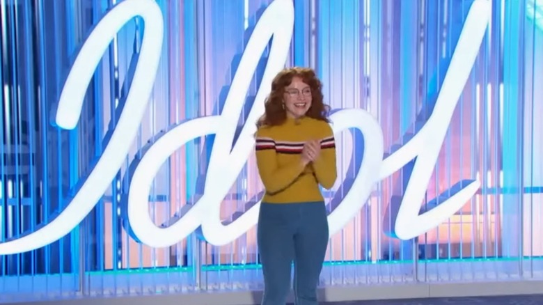 Sarah Beth Liebe in front of a big Idol sign clasping her hands happily