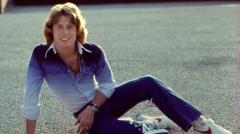 Andy Gibb (circa early 1970s) half lying on the ground with a blue and white shirt.