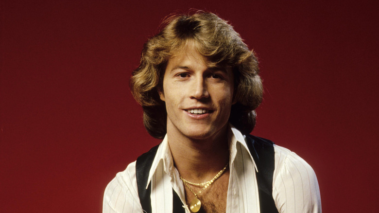 Portrait of Andy Gibb wearing a white shirt, black vest, and a gold necklace