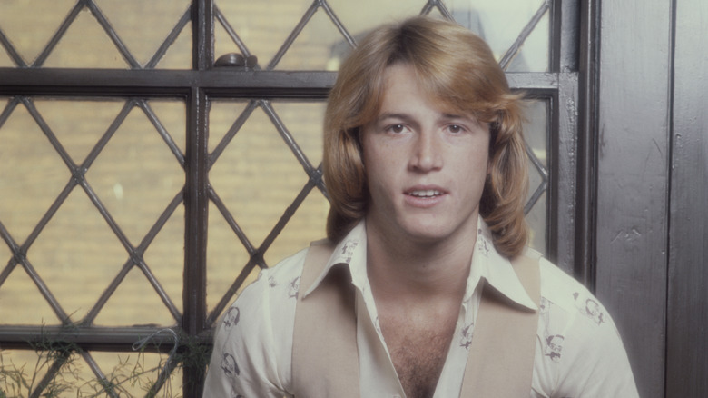 Andy Gibb posing for a photo (in a white shirt and tan vest) in 1980