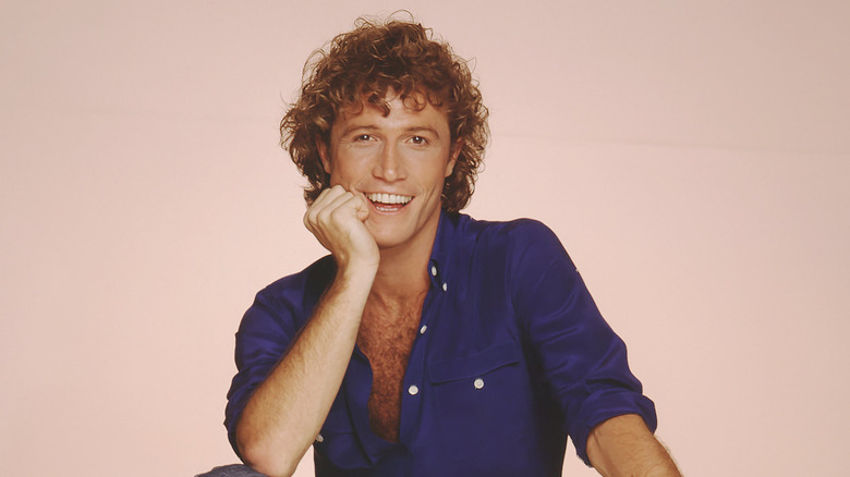 Andy Gibb posing (circa 1981) in an open blue shirt against a light pink background