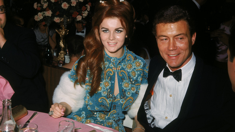 Ann-Margret wearing a teal dress and jacket with pattern embellishments, next to Roger Smith in a tuxedo