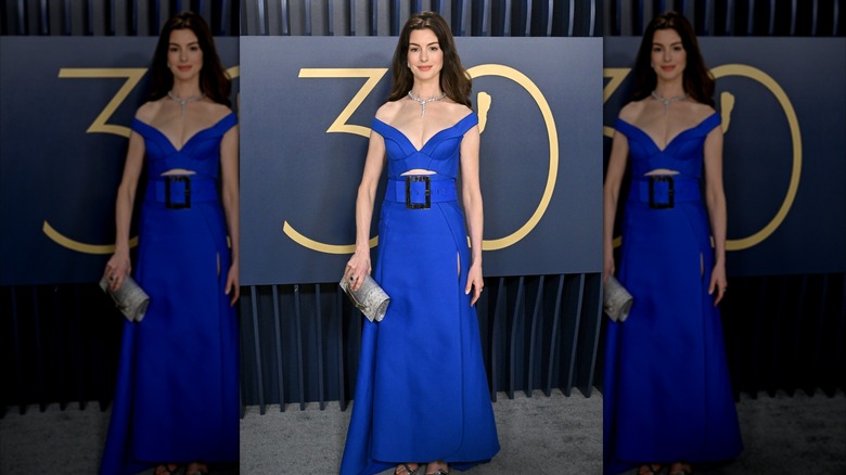 Anne Hathaway posing in a blue dress with a big belt