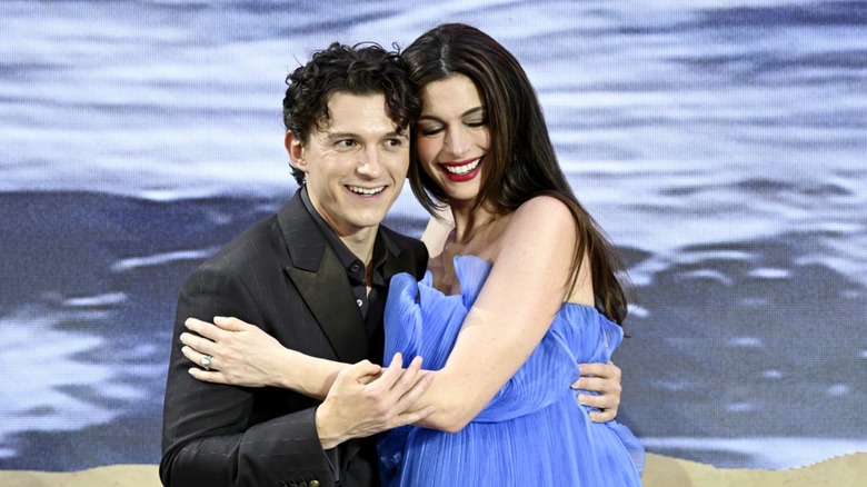 Tom Holland in a black suit hugging Anne Hathaway who is wearing a blue dress