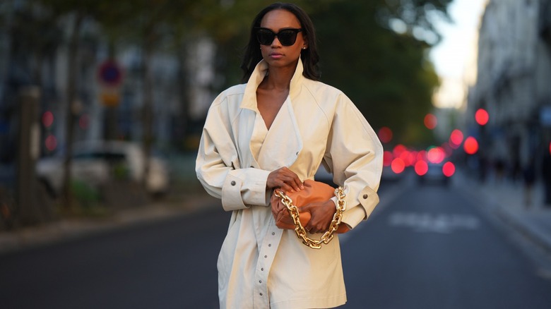 Woman in white coat and sunglasses walks
